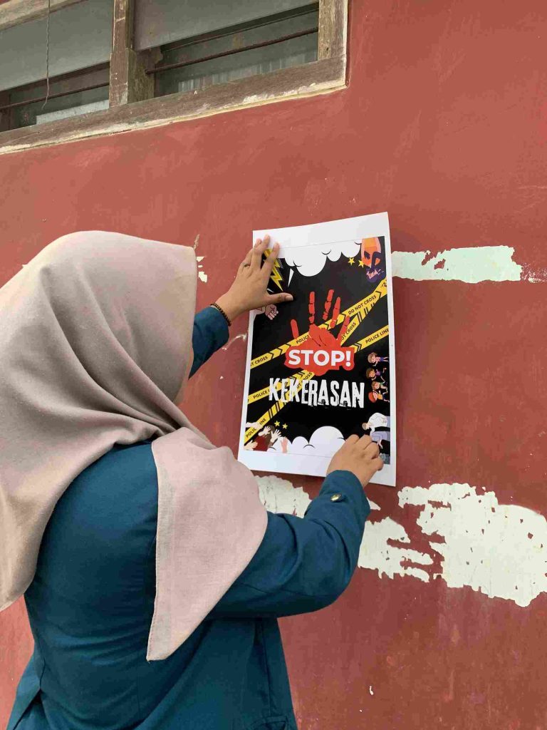 Mahasiswa KKN Kampung Baru memasang poster “Stop Kekerasan” di lingkungan Kelurahan Kampung Baru sebagai kampanye sosial.